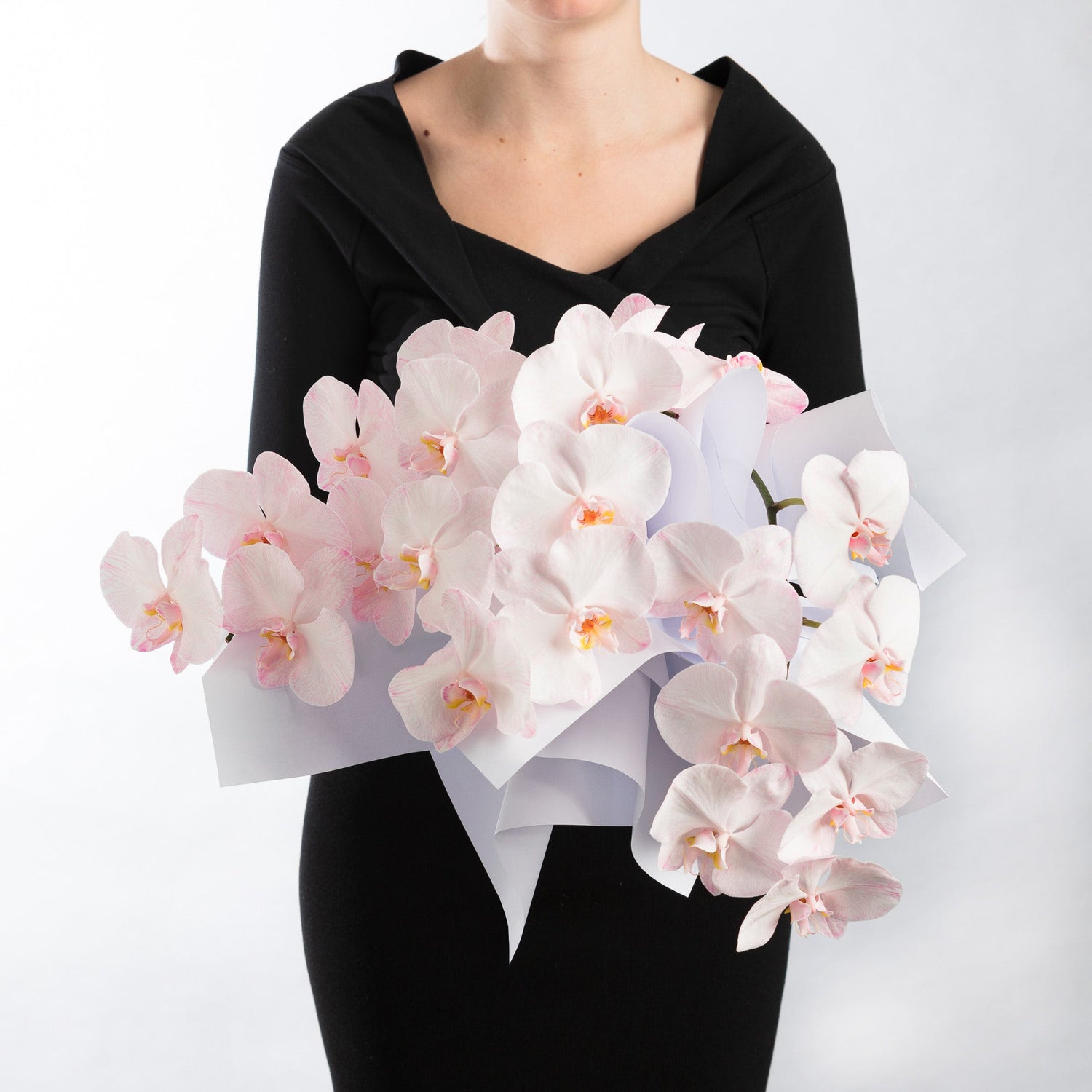 A woman earing black, holding a bouquet of soft pink phalaenopsis orchids in a bouquet.