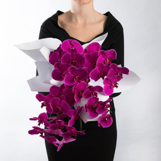 Woman wearing a black dress, holding a bouquet of deep pink phalaenopsis orchids.