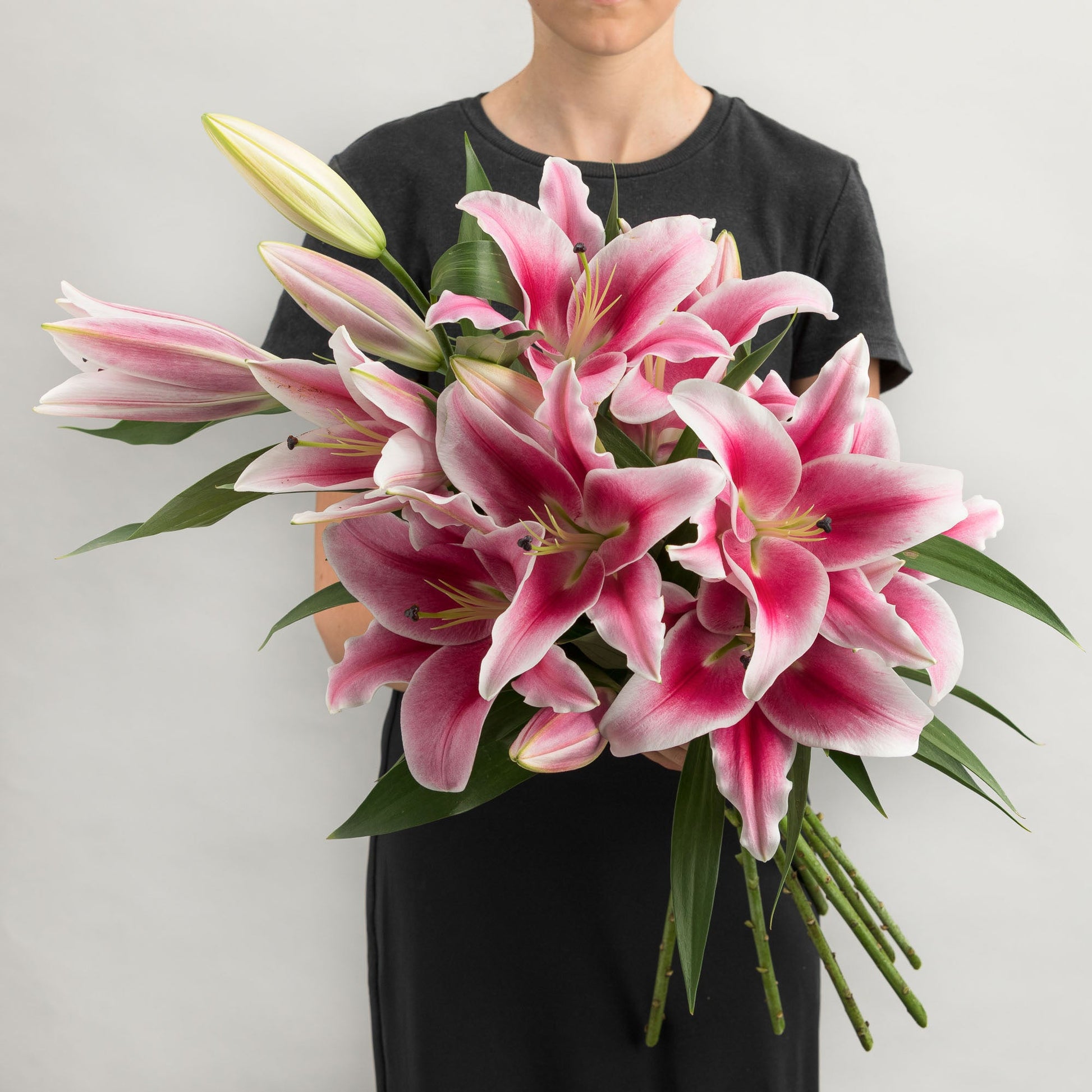 Woman wearing a black dress, holding a bouquet of pink oriental lilies.