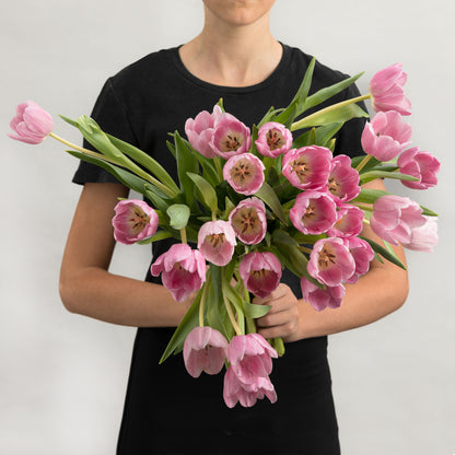 Woman wearing a black dress, holding a bouquet of soft pink tulips.