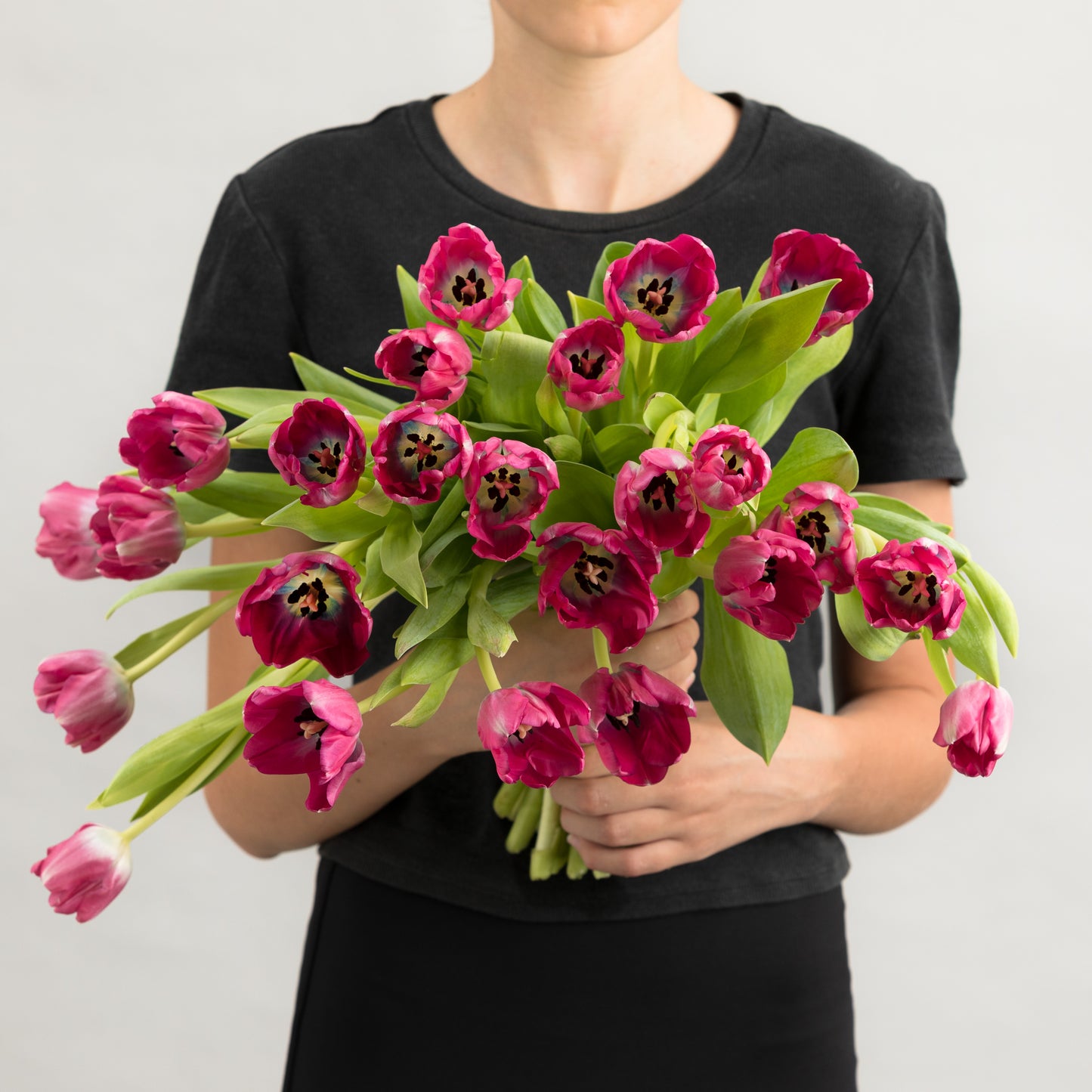 Woman wearing a black dress, holding a bouquet of hot pink tulips.