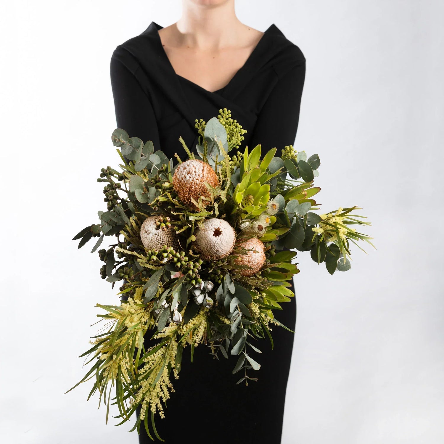 A woman earing black, holding a bouquet of Australian native wildflowers  in a bouquet.