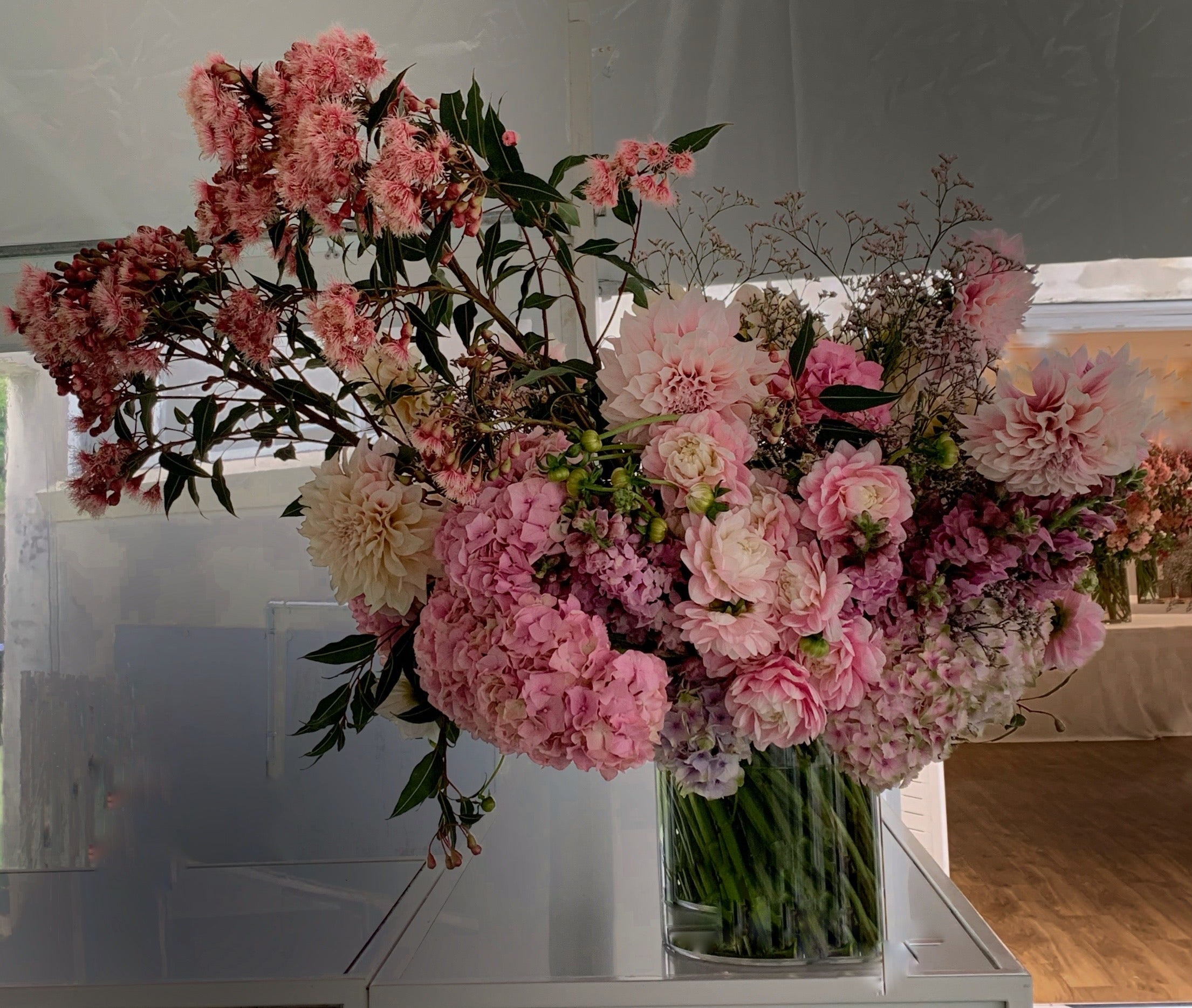 A large bunch of designer pink flowers in a glass vase at an event.