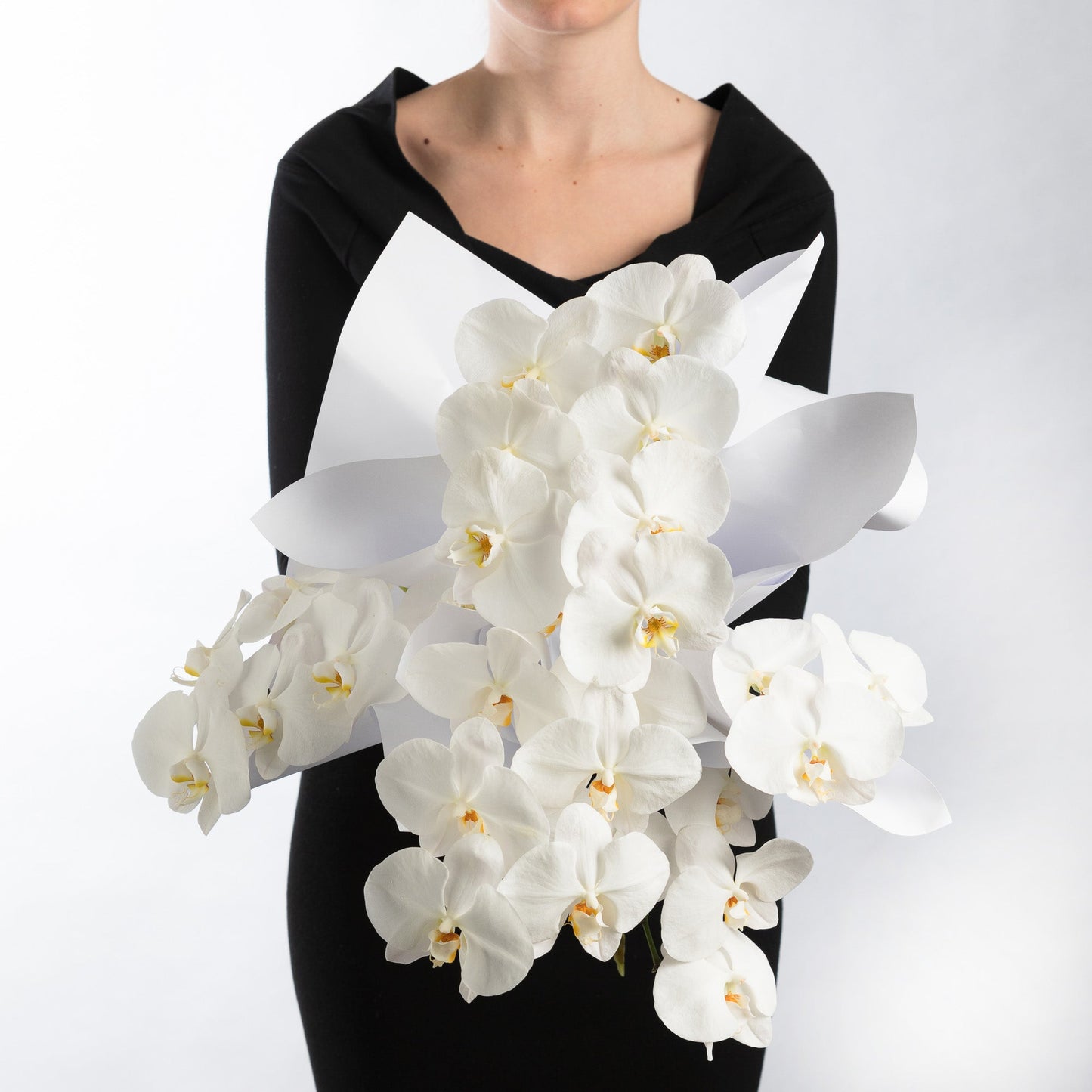 Woman wearing a black dress, holding a bouquet of white phalaenopsis orchids.