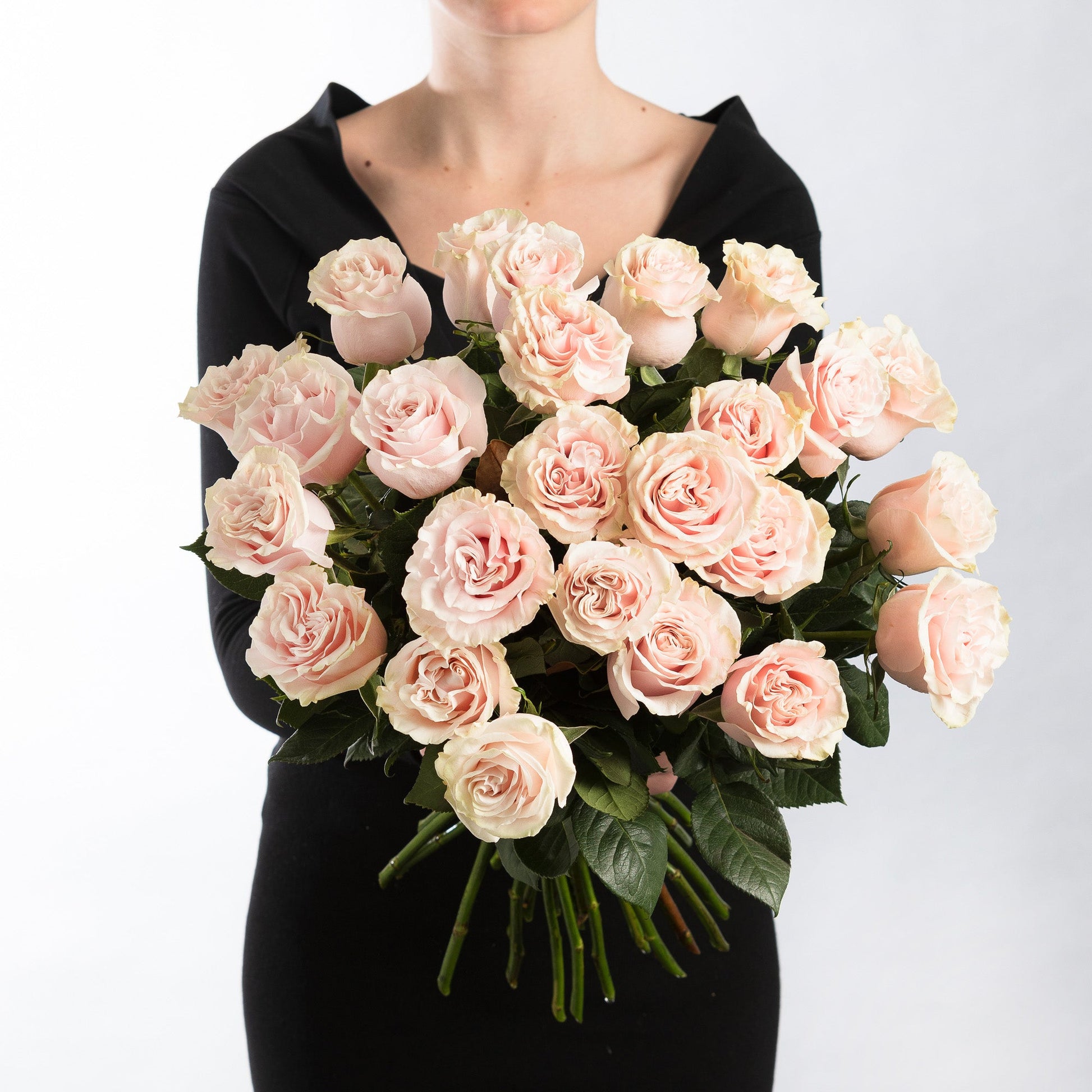 Woman wearing a black dress, holding a bouquet of premium soft pink roses.