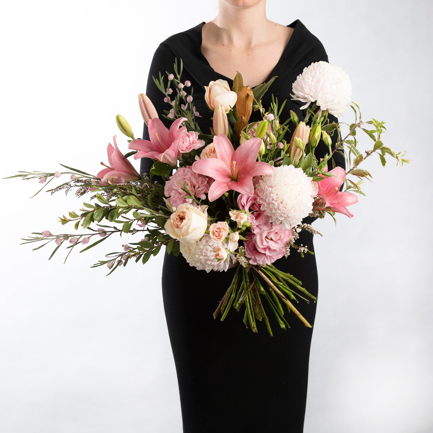 Woman wearing a black dress, holding a bouquet of mixed flowers including, tiger lilies, roses and disbud chrysanthemums in soft pinks.