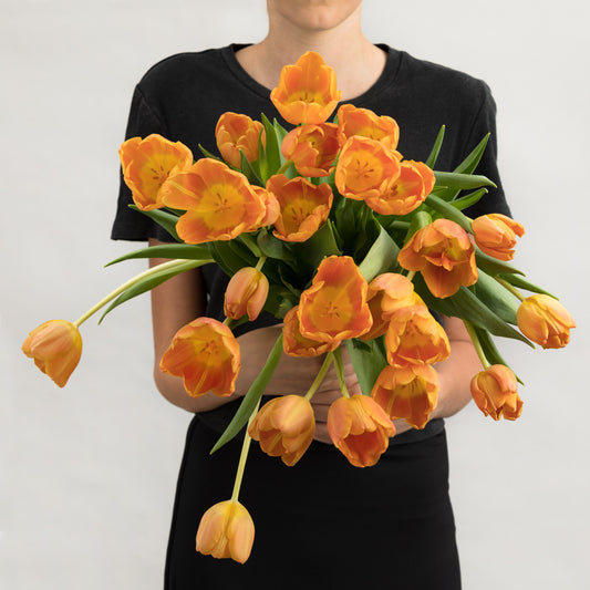 Woman wearing a black dress, holding a bouquet of bright orange tulips.